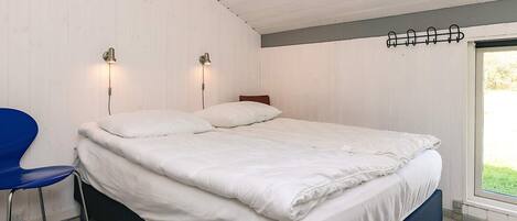 Un dormitorio con una cama, dos lámparas de pared, un sillón azul y un ventanal.