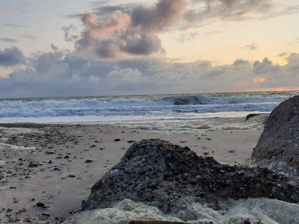 A beach with waves, pebbles, and a large rock formation.