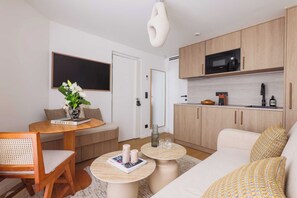 Egy modern nappali, amelyben található egy kanapé, egy dohányasztal, egy étkezőasztal székekkel, egy konyhasarok mikrohullámú sütővel, valamint egy nagy tükör.