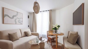 Un soggiorno moderno con un divano beige, un tavolo rotondo in legno e un piccolo tavolino da caffè. Si nota un quadro appeso al muro e una pianta in vaso sul tavolo.