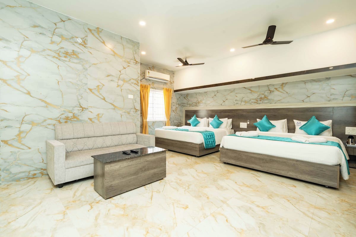 A hotel room with two beds, a sofa, a coffee table, marble walls, and ceiling fans.