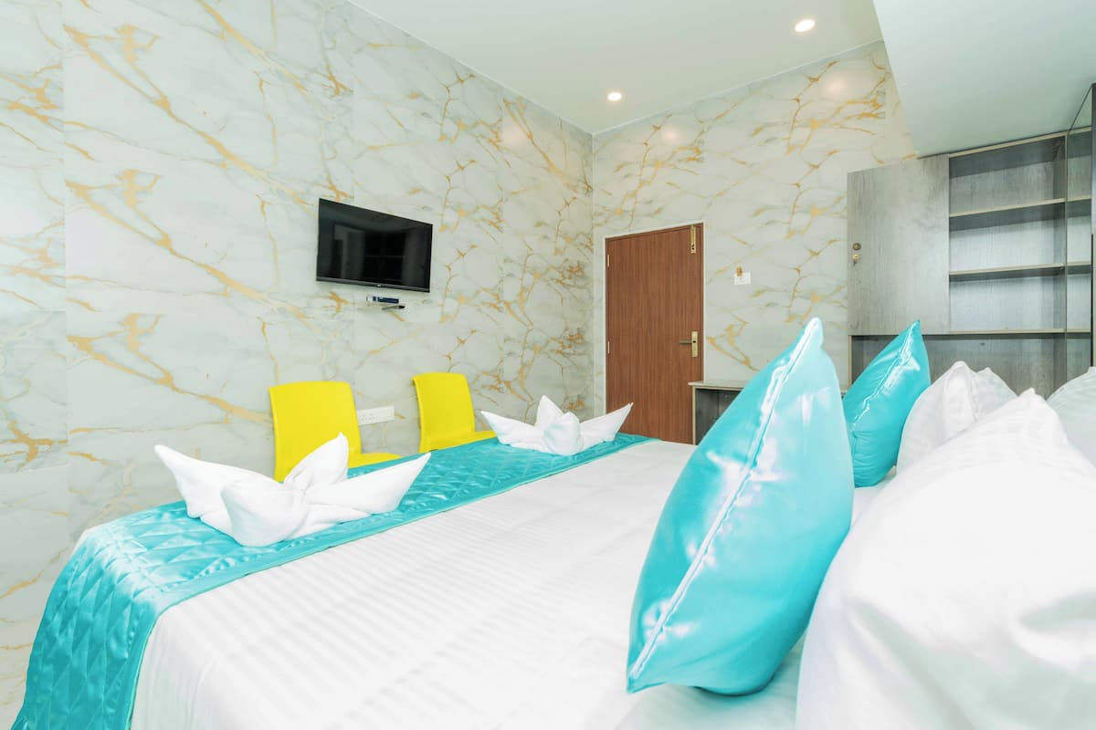 A hotel room with a marble-patterned wall, a bed with white and blue bedding, a flat-screen TV mounted on the wall, and a wooden wardrobe.