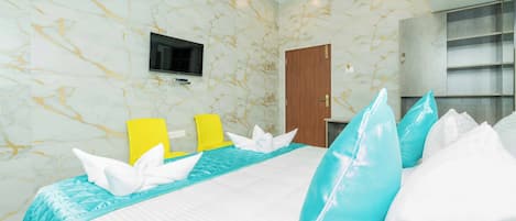 A hotel room with a marble-patterned wall, a bed with white and blue bedding, a flat-screen TV mounted on the wall, and a wooden wardrobe.
