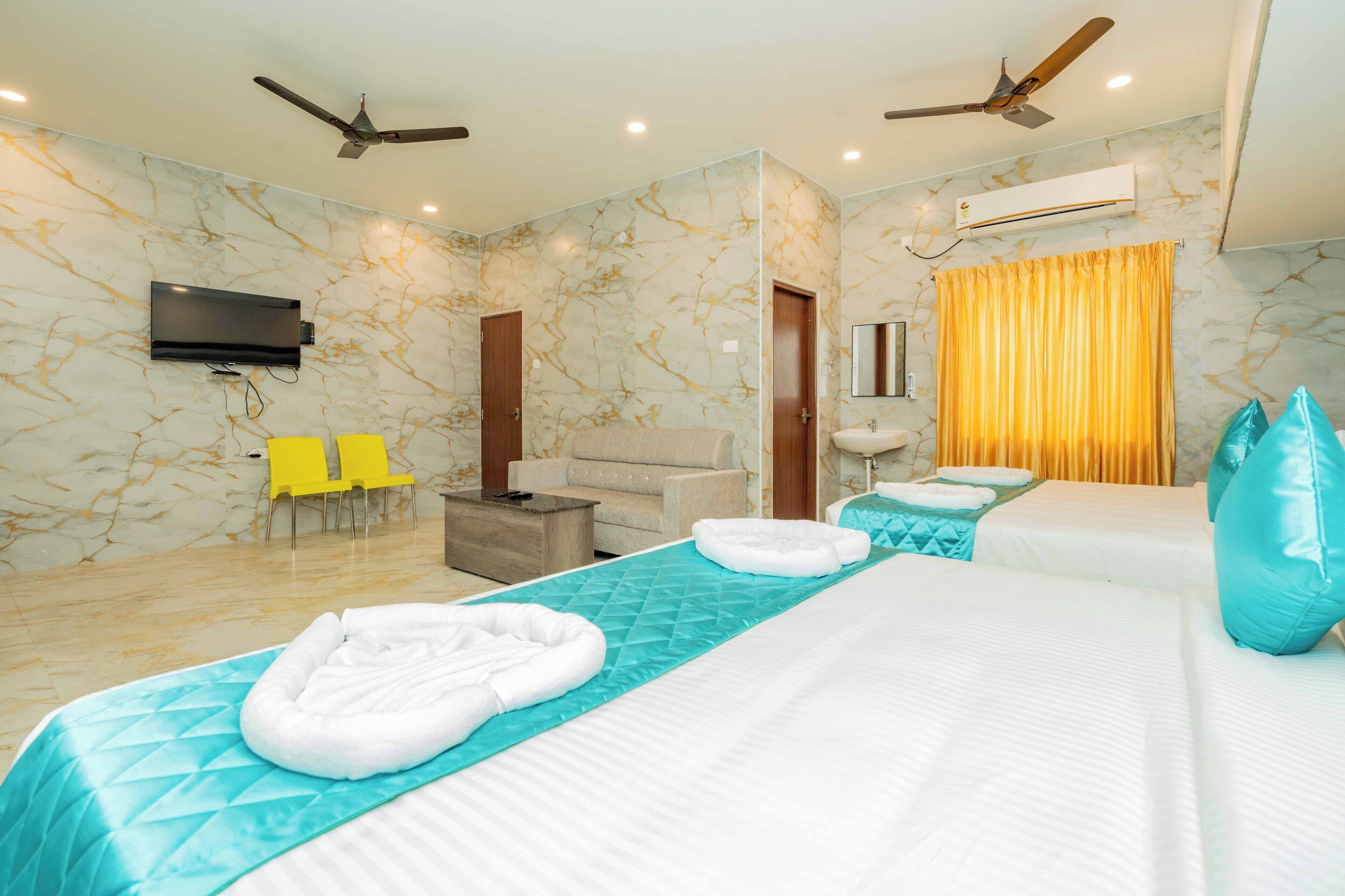 Habitación de hotel con dos camas, televisor, ventiladores de techo, sofá y baño con espejo y cortina.