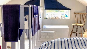 Ein Zimmer mit einem Etagenbett, einem Fenster mit Aussicht, einem Stuhl und einer kleinen, weißen Kommode.