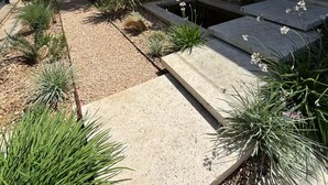 A landscaped garden with various plants and a stone pathway leading to a building with a stone facade. - Magnificent contemporary & design villa (Saussan)
