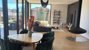 A modern living room with a round wooden table, dark green chairs, a sofa, and a large window offering a view of the outdoors. - Magnificent contemporary & design villa (Saussan)