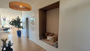 A modern interior with a wooden floor, a large hanging light fixture, a seating area with cushions, and a potted plant. - Magnificent contemporary & design villa (Saussan)