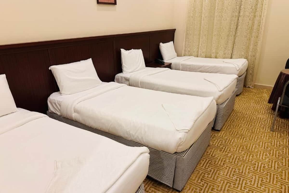 Une chambre d’hôtel avec trois lits simples, une tête de lit en bois, une moquette à motifs et un rideau.