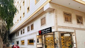 Exterior del Hotel Verita, con una entrada de mármol y un coche rojo estacionado frente a él.