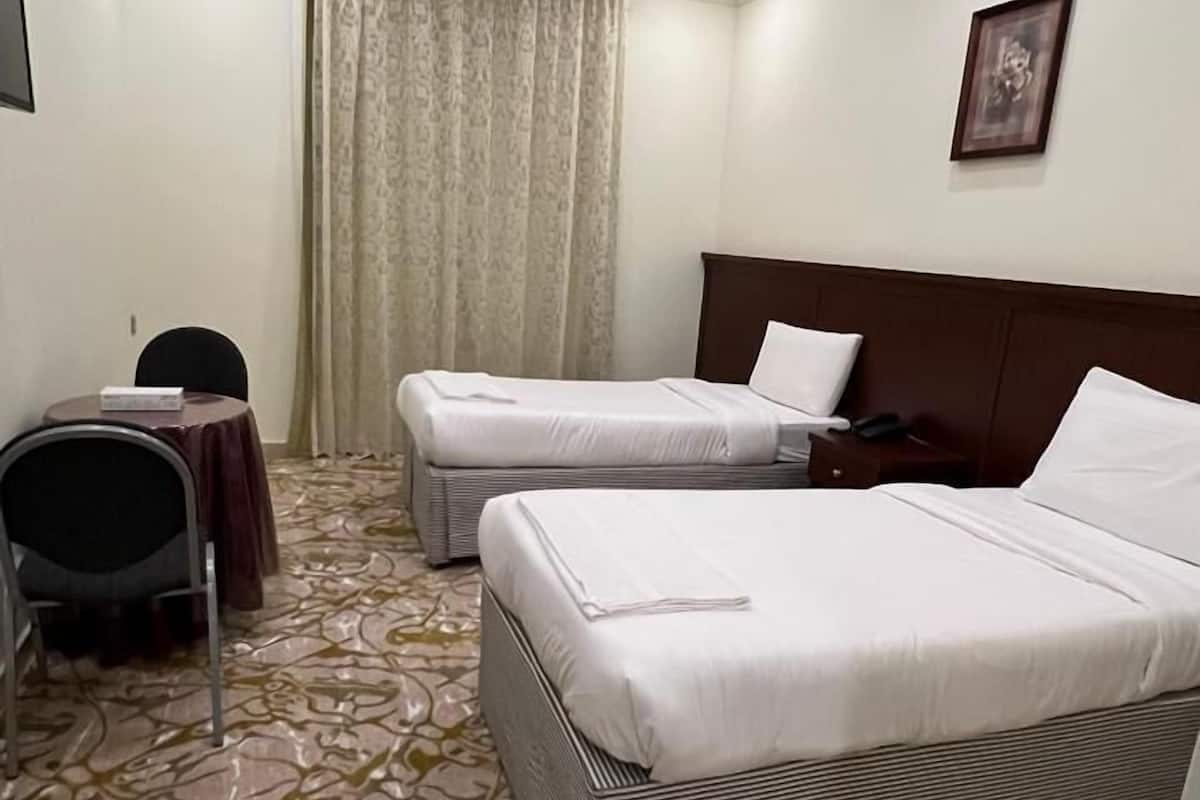 Une chambre d’hôtel avec deux lits simples, un bureau avec une chaise, une grande fenêtre avec des rideaux et un tapis à motifs.