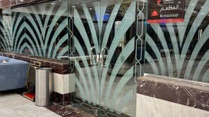 Zona de recepción con mostrador de mármol, separador de vidrio con diseño de hojas y cartel de restaurante.