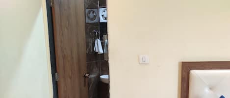 A hotel room with a bed, a nightstand with a kettle, slippers, and a door leading to a bathroom.