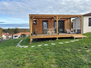 A wooden deck with outdoor furniture, a glass door entrance, and a view of the landscape. - Tiny House with Jacuzzi on terrace, view of Limoges. (Feytiat)