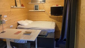 A small, cozy room with wooden walls, a bed, a desk, and a television. - Tiny House with Jacuzzi on terrace, view of Limoges. (Feytiat)