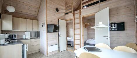 A compact, modern kitchen with built-in appliances, a dining area with a table and chairs, and a loft bedroom with a ladder.