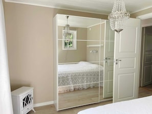 A bedroom with a mirrored wardrobe, a bed with a white bedspread, a small bedside table, and a chandelier. - 4 Star Holiday Home in Sollentuna (Sollentuna)