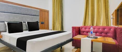 A hotel room with a bed, a red sofa, a small wooden table, and yellow curtains.