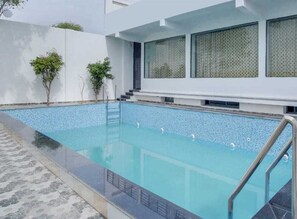 A modern indoor swimming pool with clear blue water, surrounded by a tiled deck and a white building facade. - Shree Ji Hotel & Banquet (Karnal)