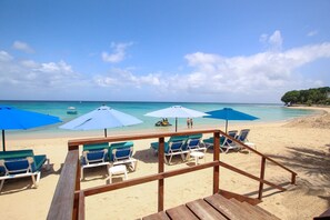 Una spiaggia con ombrelloni azzurri, lettini e un molo di legno.
