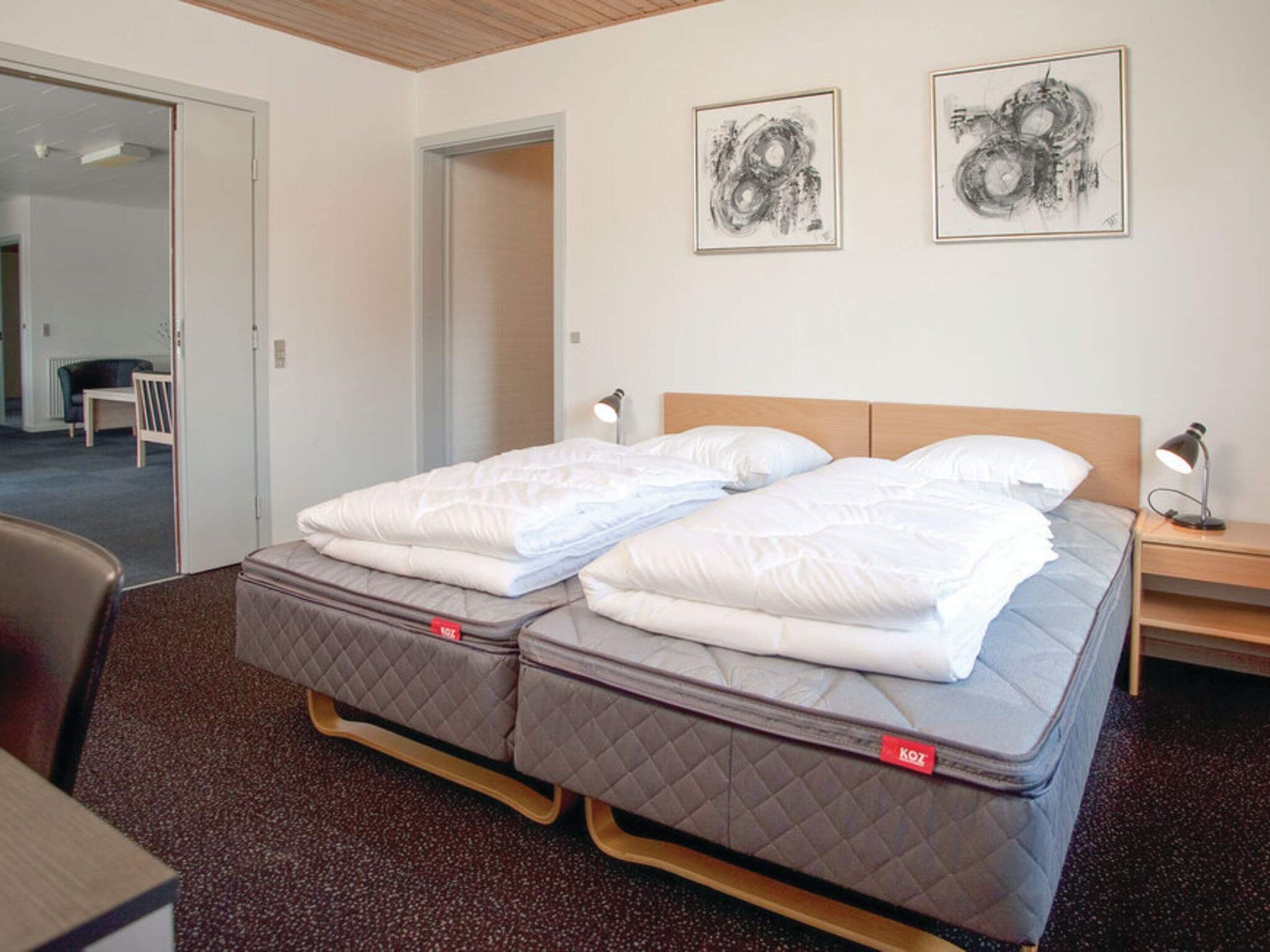 A double bed with two pillows, a bedside table with a lamp, and two framed artworks on the wall.
