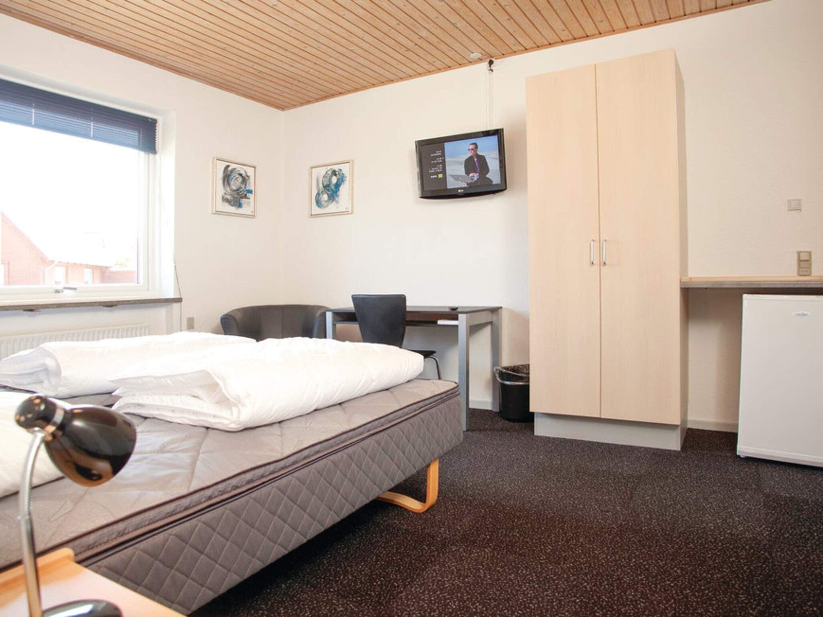 Een hotelkamer met een bed, bureau, stoel, garderobe en een televisie.