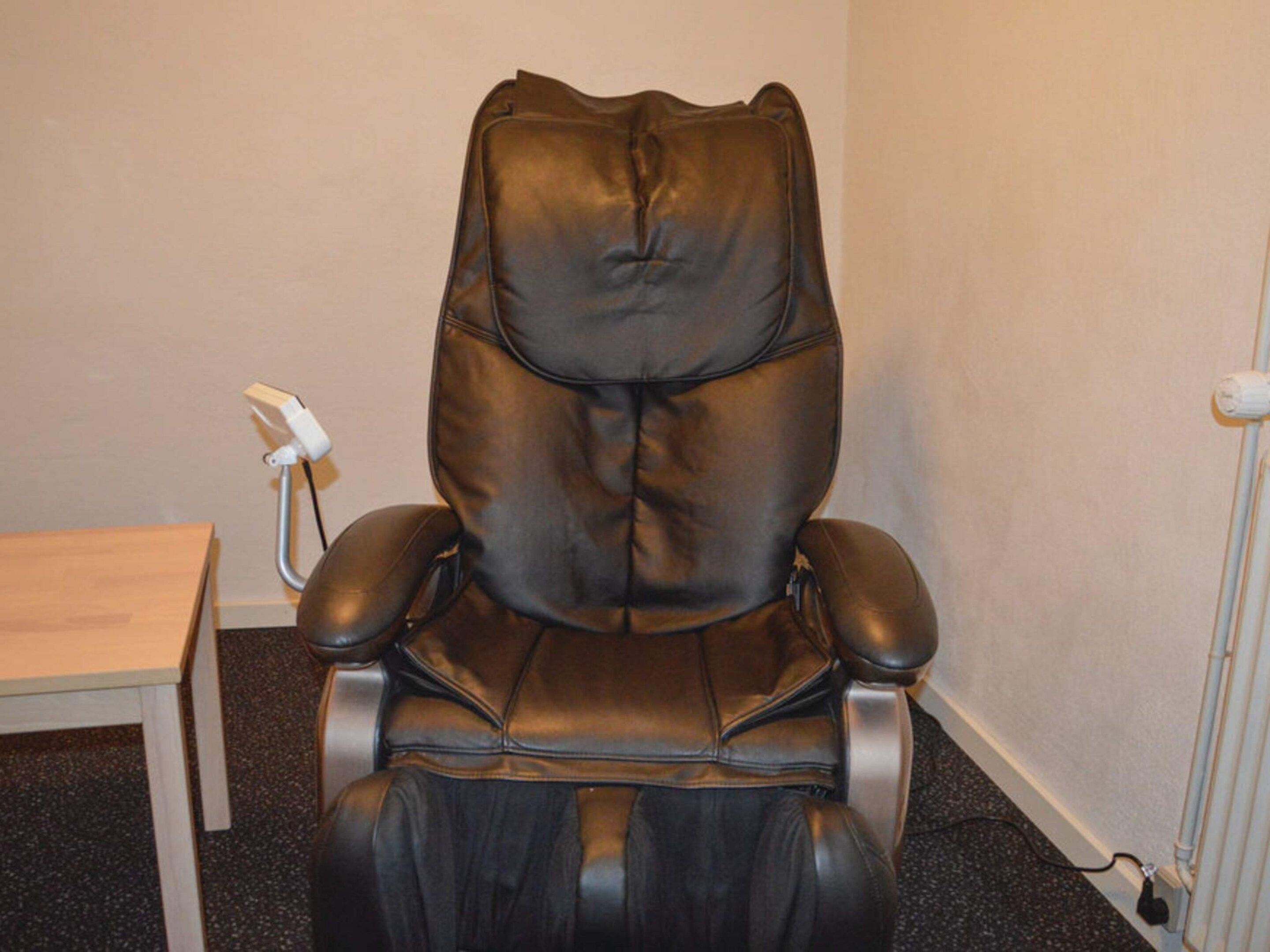 A massage chair with a control panel, a small table, and a radiator in a room.
