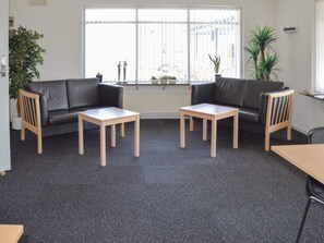 A room with two black leather sofas, two wooden tables, and a radiator. - 5 Star Holiday Home in Thyboron (Thyborøn)