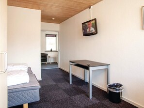 Een kleine, eenvoudig ingerichte kamer met een bed, een tafel, een stoel en een prullenbak.