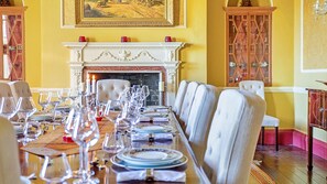 Uma sala de jantar formal com uma mesa longa posta para refeição, lareira e armários de madeira tradicional.
