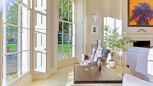 A spacious living room with large windows, a fireplace, and a view of a garden.