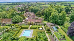 A large estate with a swimming pool, manicured gardens, and a variety of buildings including a main house and several outbuildings.
