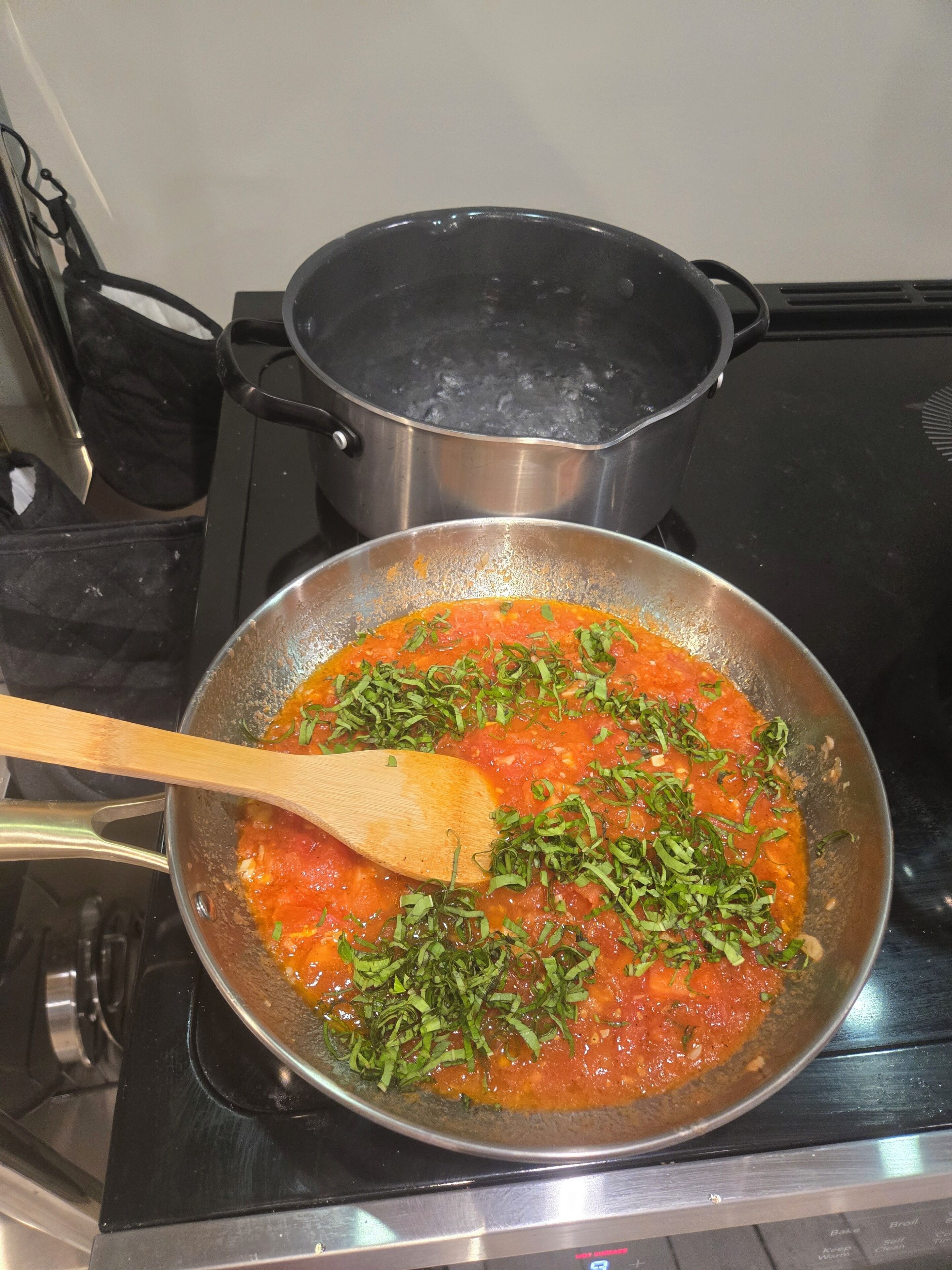 Une cuisine avec un fourneau, une poêle contenant une sauce et une casserole sur le fourneau.