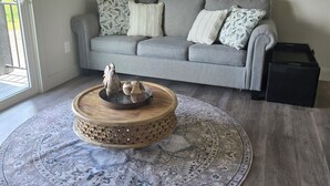 A living room with a grey sofa, patterned cushions, a round wooden coffee table with decorative items, a large woven tapestry, and a patterned rug on a wooden floor. - Charming 1-bedroom farmhouse in marvelous Seneca with WiFi, AC (Seneca)