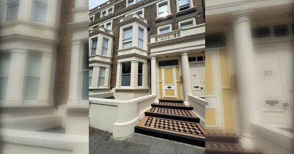 Un immeuble à plusieurs étages, de style architectural traditionnel, avec une entrée imposante et un escalier menant à une porte marquée du numéro « 52 ».
