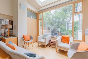 Ein modernes Wohnzimmer mit einer Couch, Sesseln, einem kleinen Tisch und einem Bücherregal.