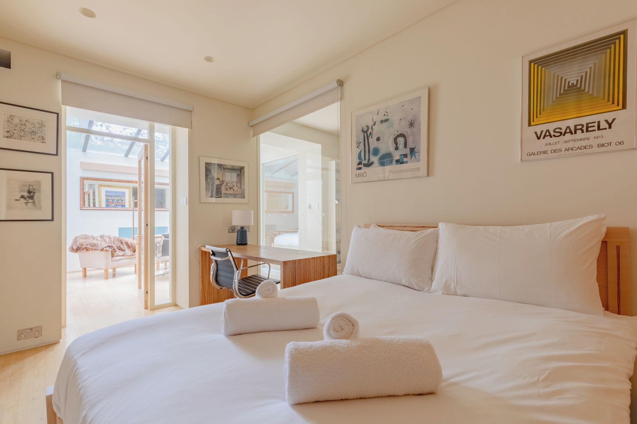 Une chambre d’hôtel avec un grand lit, un bureau et une chaise. Les murs sont ornés de tableaux encadrés et il y a une fenêtre avec vue.