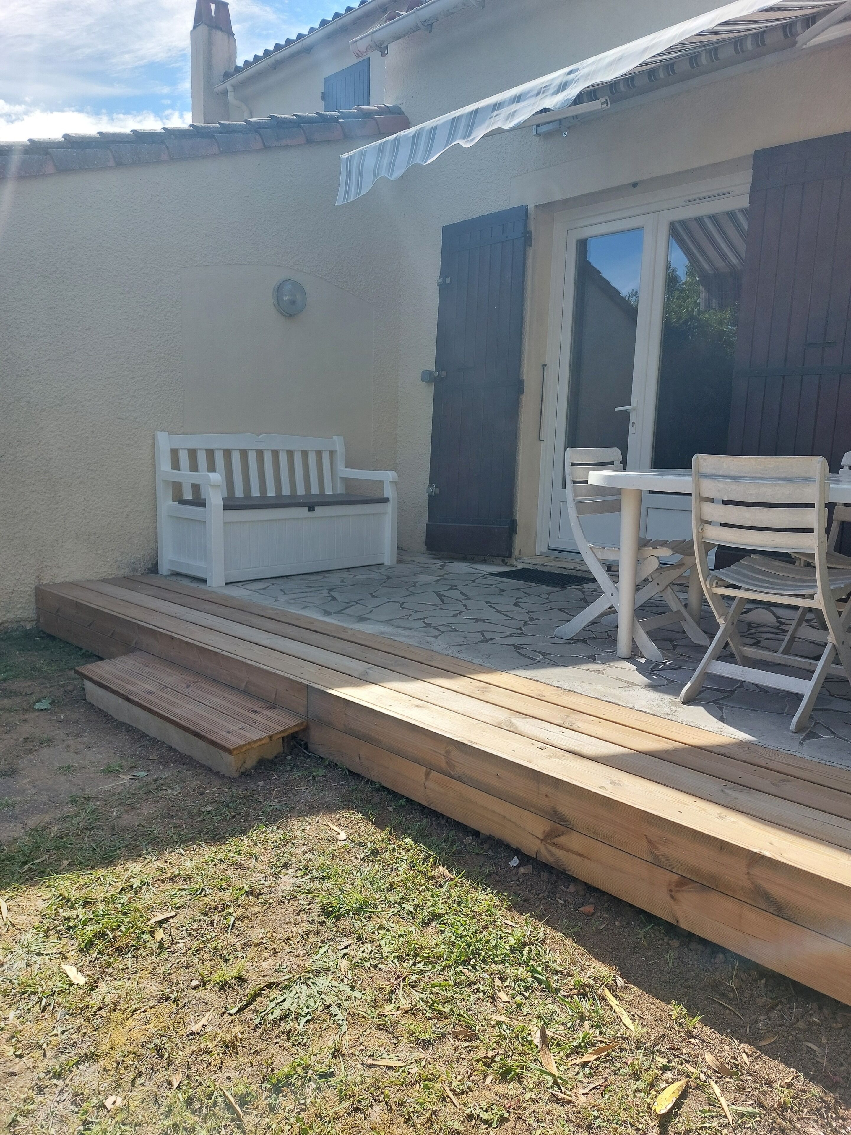 Een terras met een houten terras, een witte bank, een tafel met stoelen en een schuifdeur van glas.