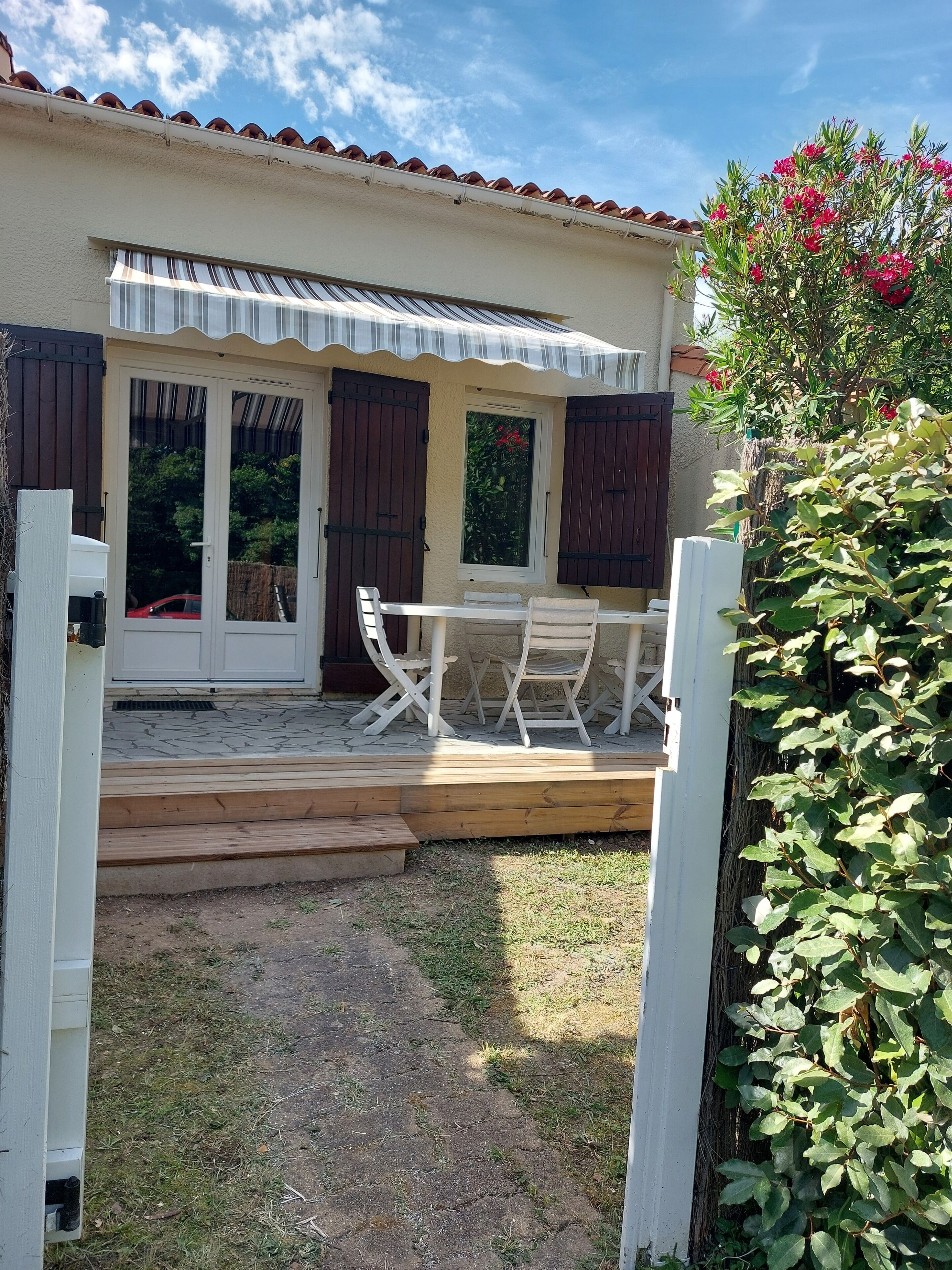 A covered patio with a table and chairs, a wooden deck, and a garden area.