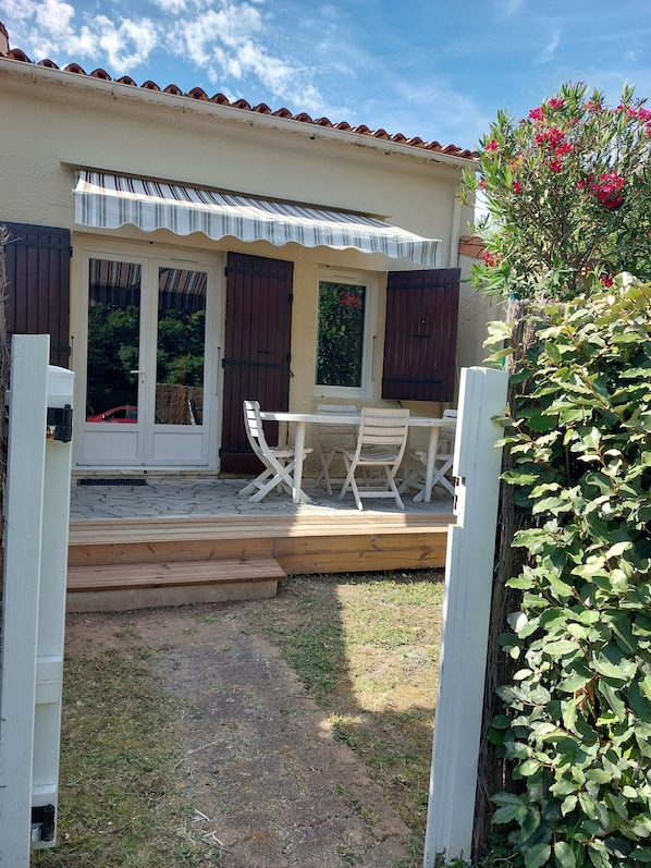 A covered patio with a table and chairs, a wooden deck, and a garden area. - House in a private hamlet near the beach (Vaux-sur-Mer)