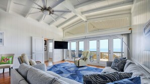 A spacious living area with a large gray sofa, a blue patterned rug, and a ceiling fan. - Peace of Heaven Three Bedroom Oceanfront Home in Long Bay Estates (Myrtle Beach)