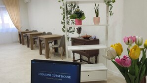 Een laptop op een bureau, met een bloevas, een plantenplank en een eethoek op de achtergrond.