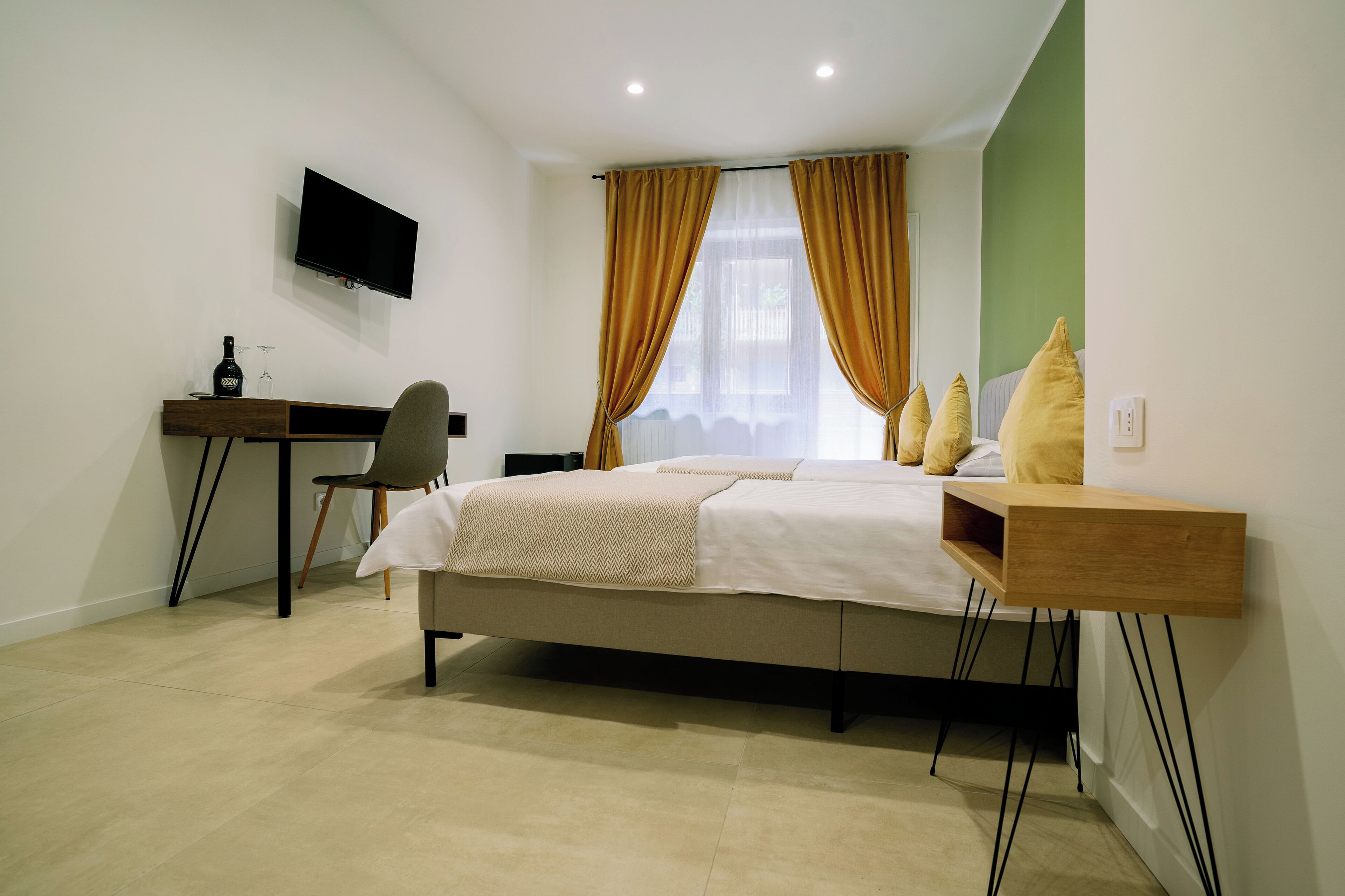 Un dormitorio con una cama, un escritorio, una silla y un televisor montado en la pared.