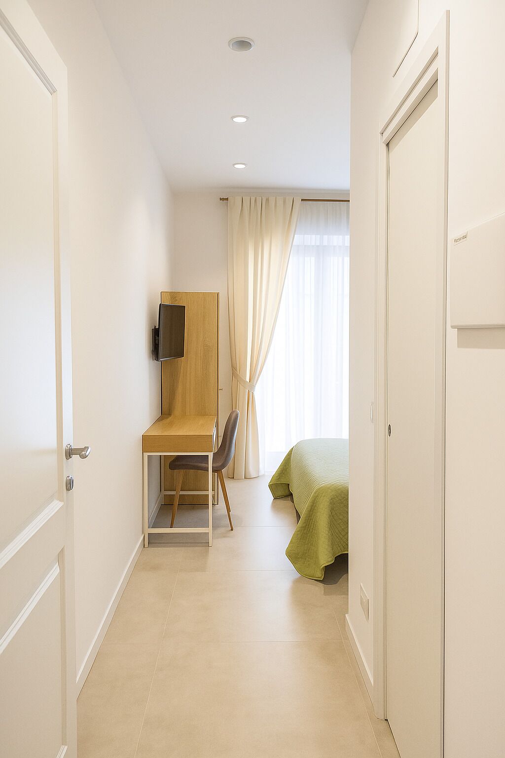 A hotel room with a desk, chair, bed, and a TV mounted on the wall.