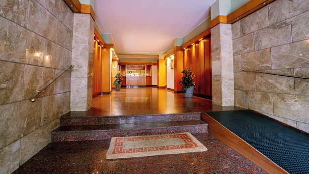 Een hotellobby met marmeren vloeren, een centraal gelegen receptiebalie en een trap naar de verdiepingen erboven.