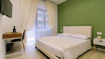 Un dormitorio con cama, escritorio, silla, televisor y ventana con cortinas.