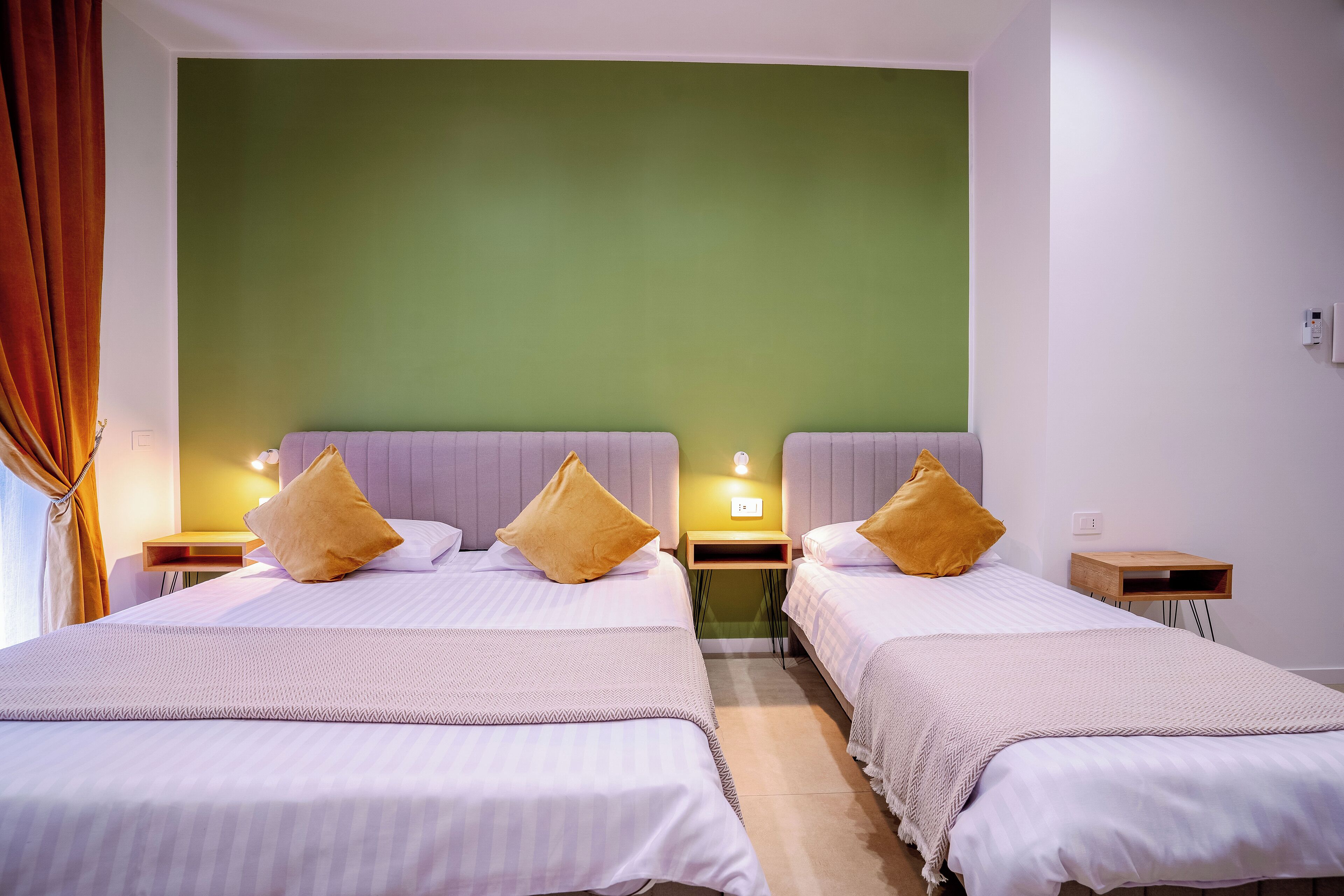 A hotel room with two beds, each with a pillow and a bedside table with a lamp.