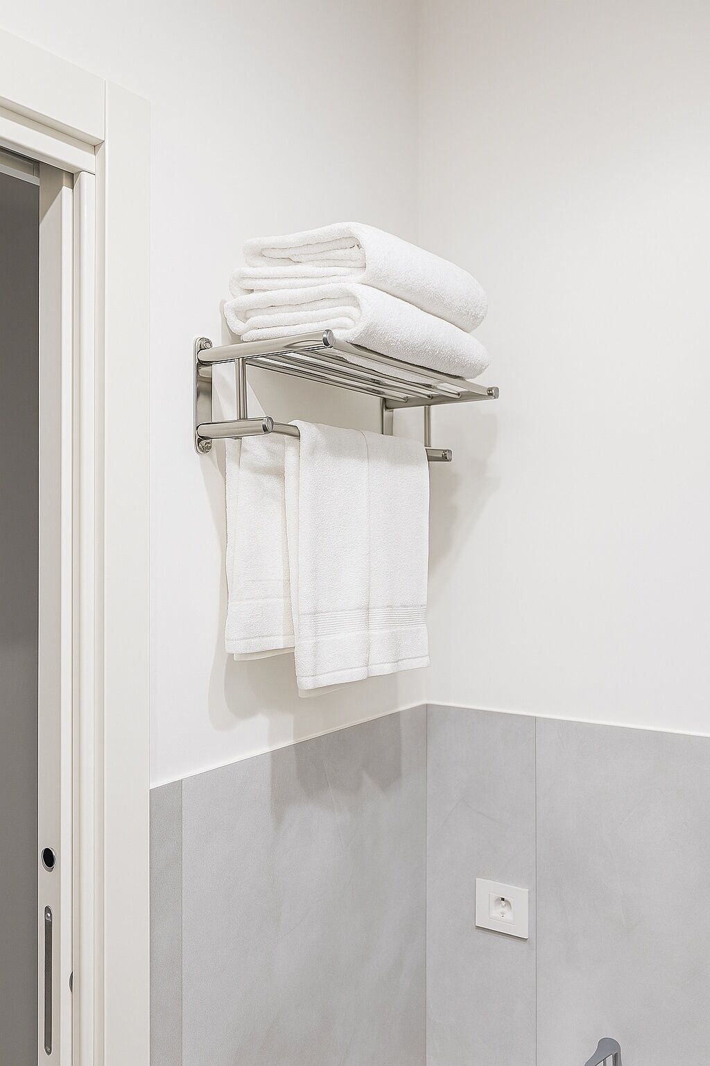 A bathroom with a towel rack holding folded towels and a visible electrical outlet on the wall.