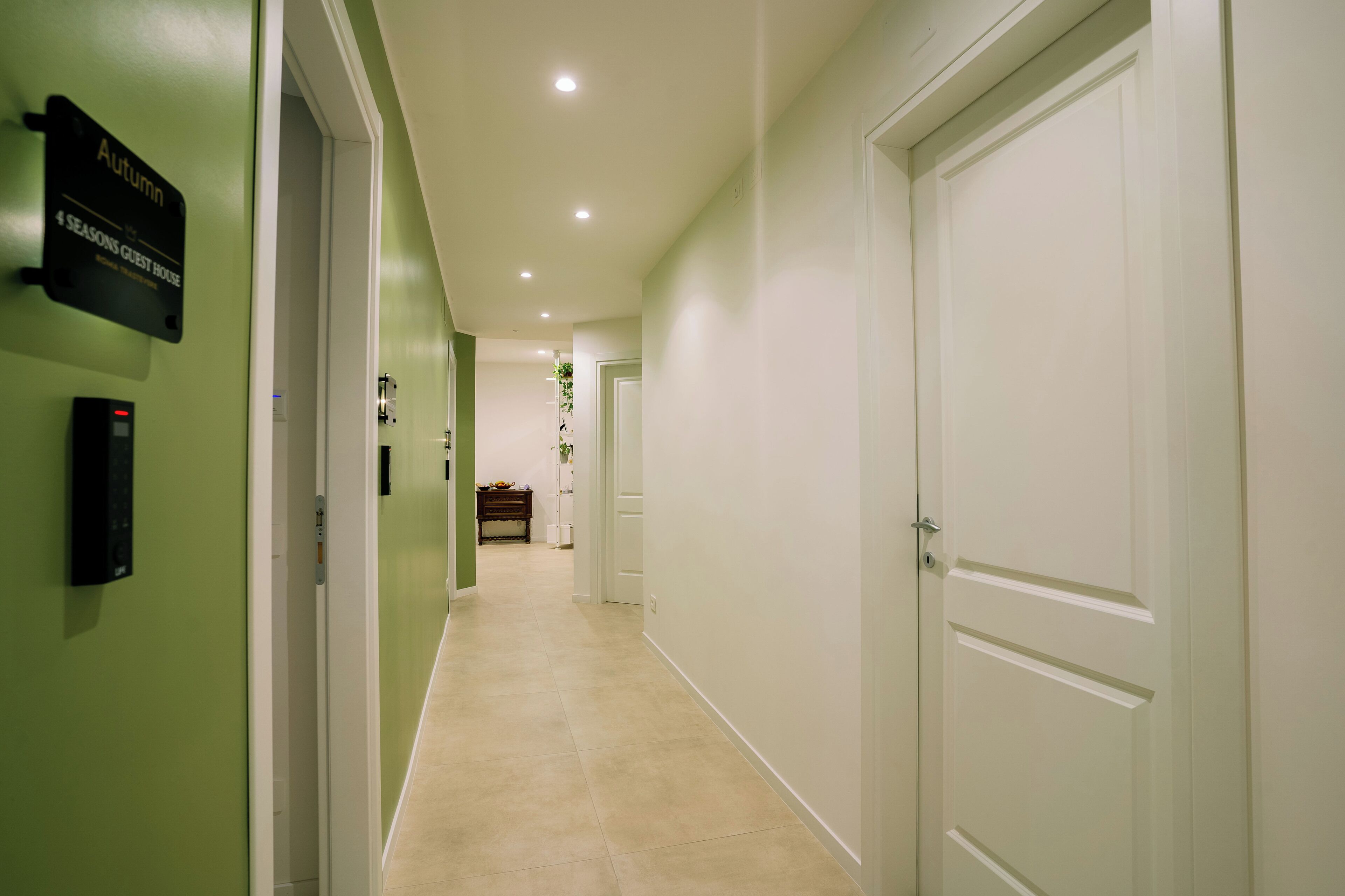 A hotel corridor with a sign indicating a guest house, a security keypad, and a door at the end.