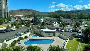 A residential area with a swimming pool, parked cars, and a view of a mountain.